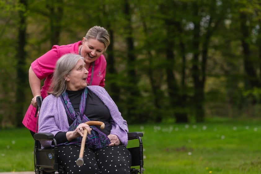 Female Home Carer walking with female client in wheelchair