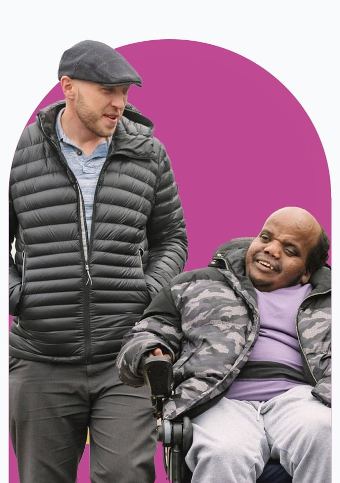 Male Mobility Care client in wheelchair with male Live-in Carer walking beside him